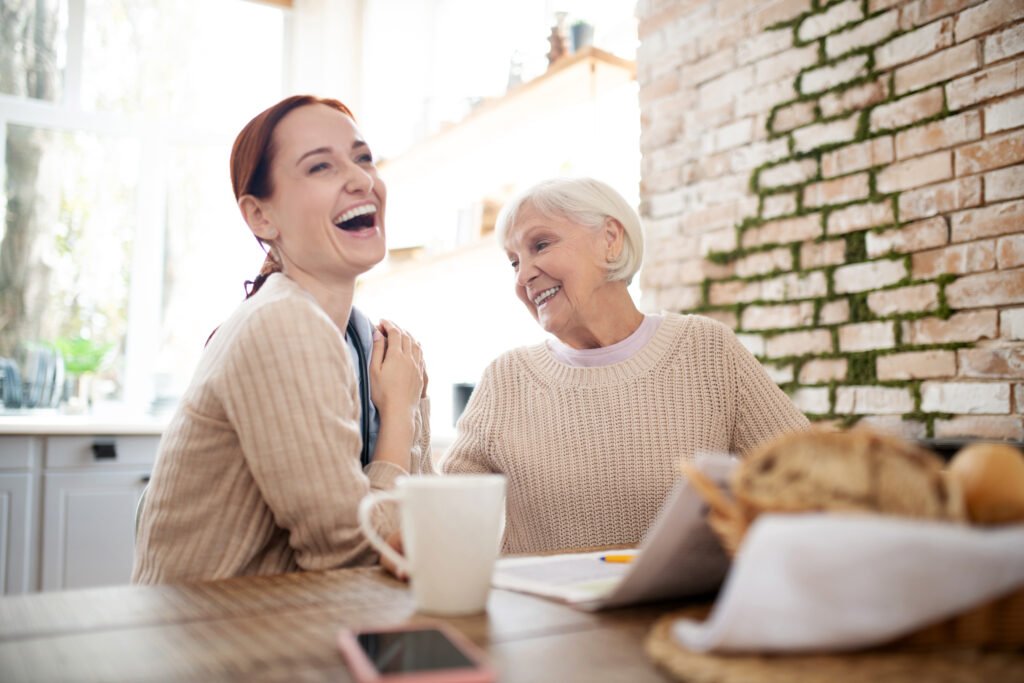 red haired caregiver laughing while pensioner joking