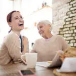 red haired caregiver laughing while pensioner joking